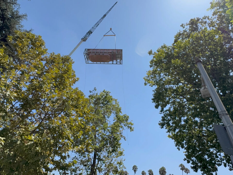 Crane lifting a pool in a transport frame between trees.