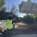 Crane lifting a 10-by-20-foot precast concrete pool shell during installation.
