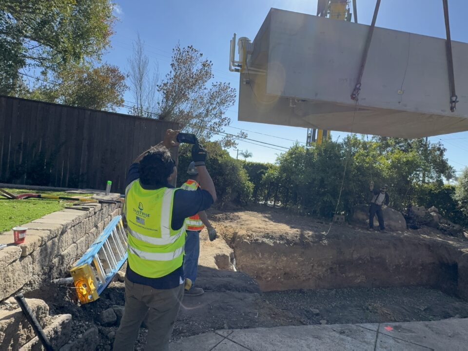 Crane lifting a 10-by-20-foot precast concrete pool shell during installation.